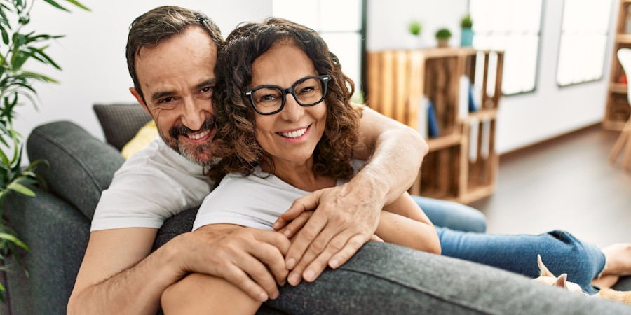 Middle age hispanic couple smiling happy sitting on the sofa with dogs at home.